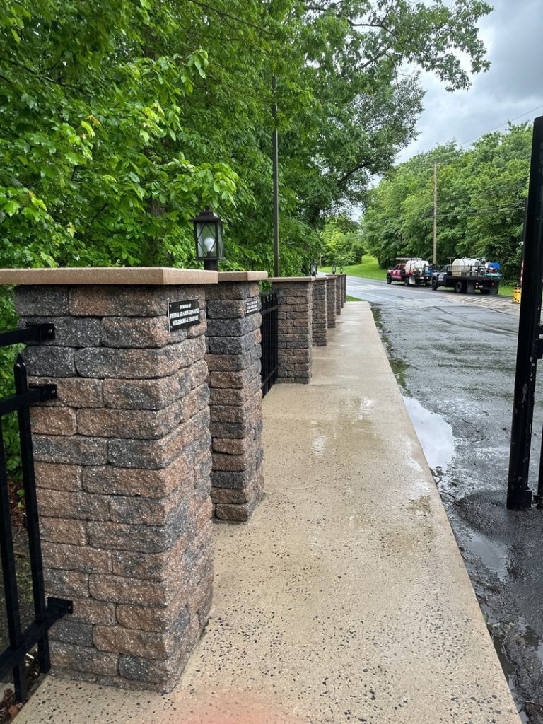 clean concrete walkway with stone pillars and greenery background showing well-maintained entrance area