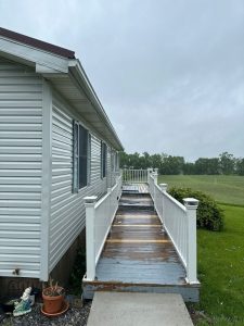cleaning a wooden walkway with visible dampness and greenery surrounding the area under overcast skies
