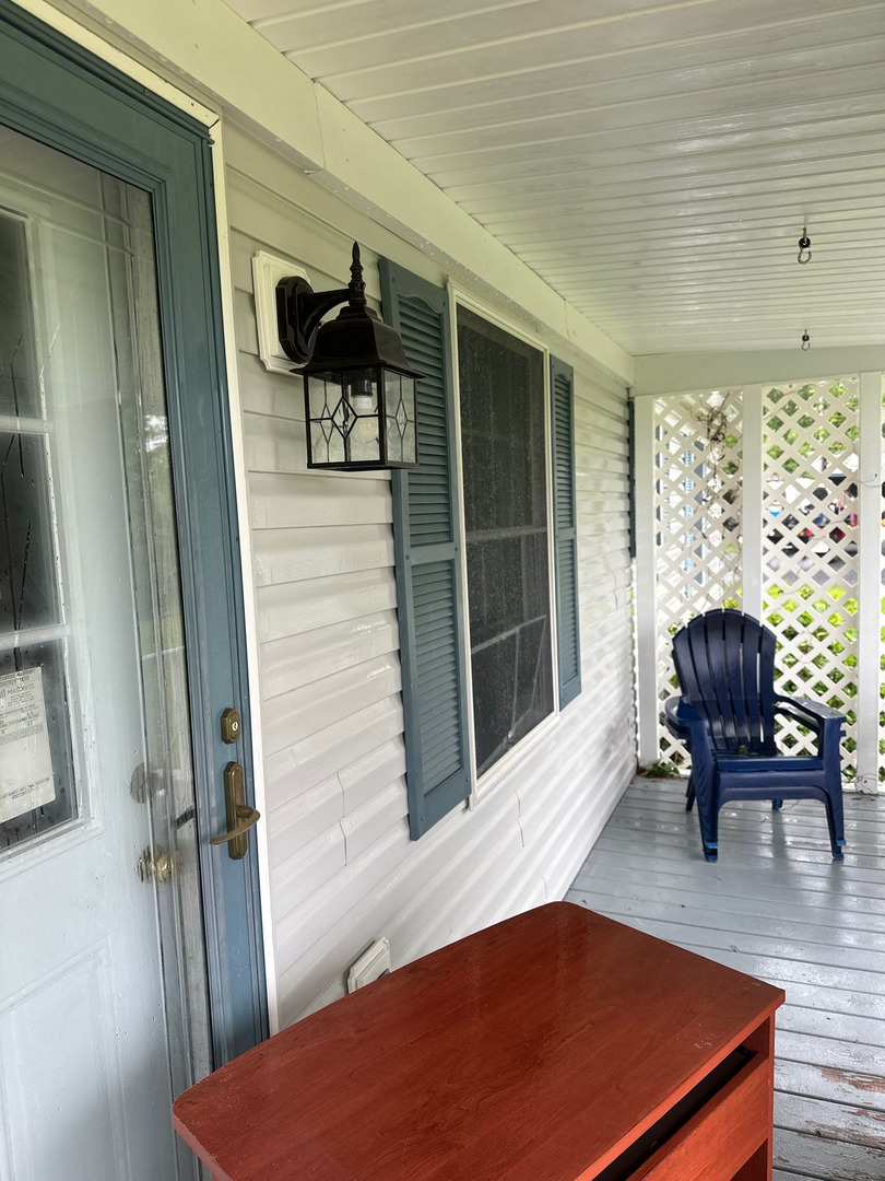 covered porch with a door and a wooden table blue chair in background and a lantern fixture on the wall