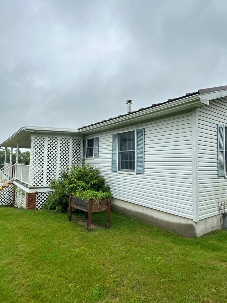 house washing on white vinyl siding with green grass and plants around the foundation and cloudy sky above